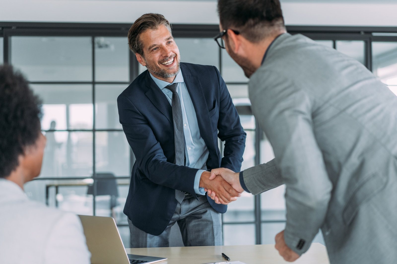 A hiring manager shaking hands with a candidate in a modern office