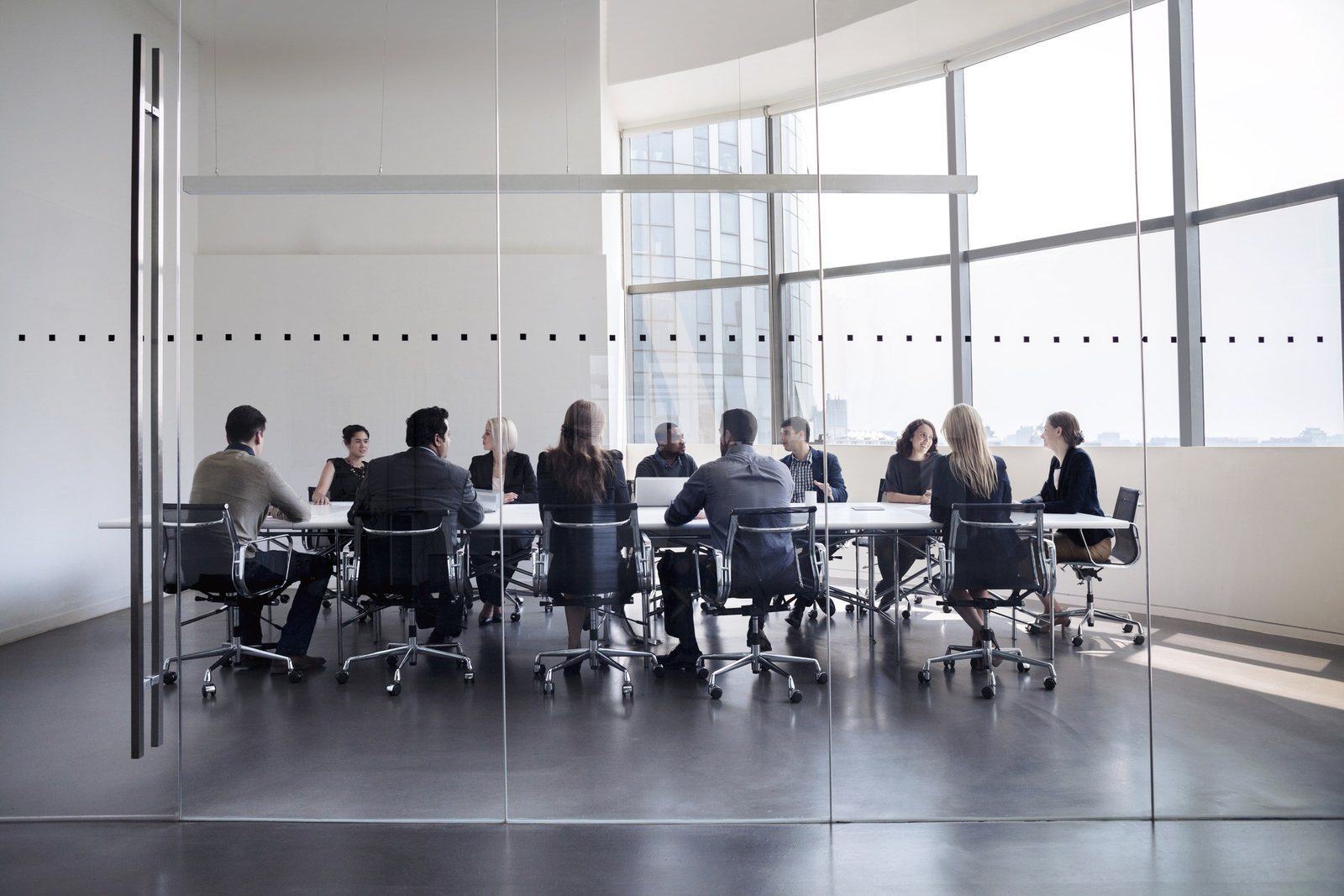 A leadership team meeting around a boardroom table in a glass-walled office